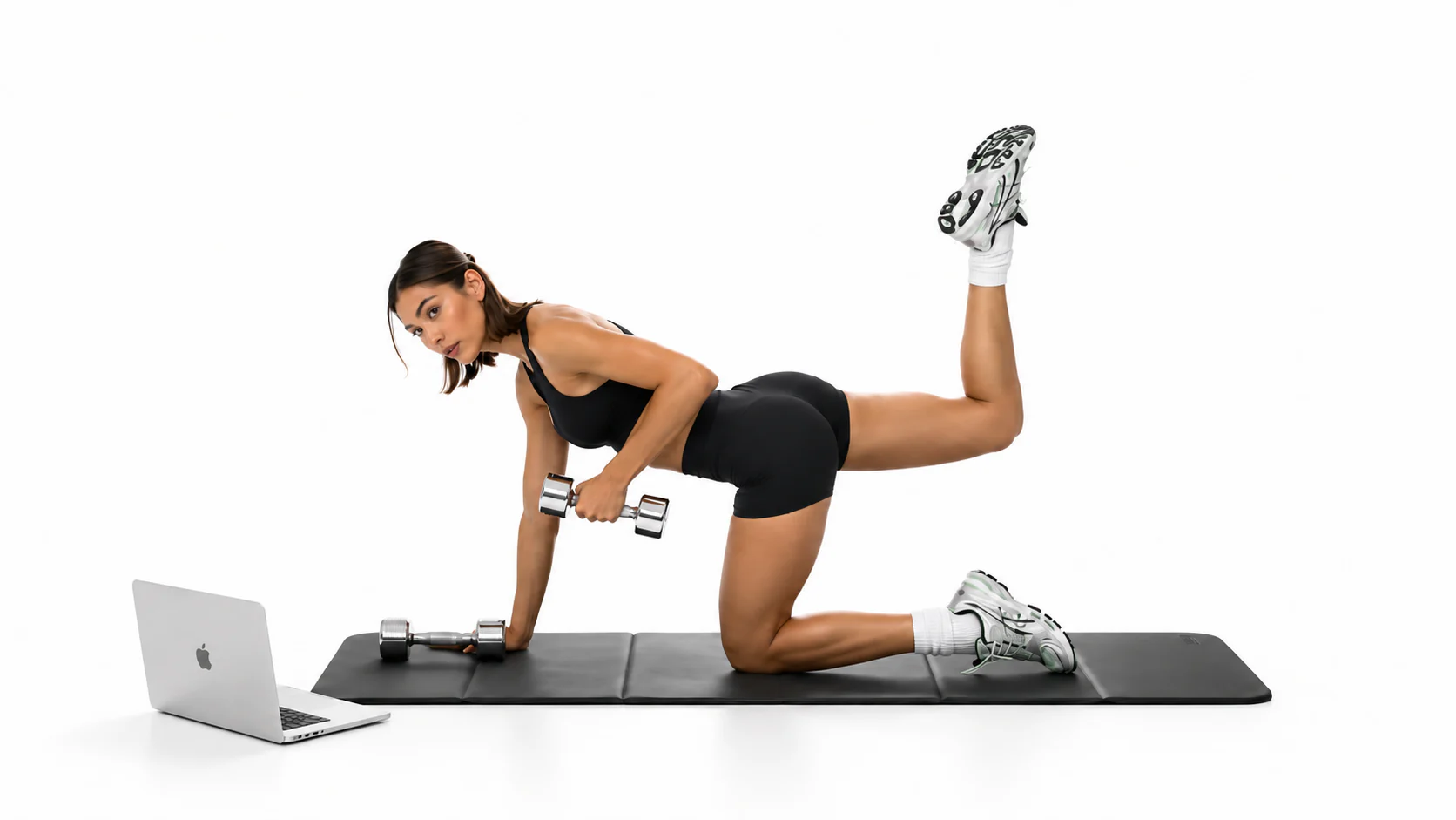 Mujer entrenando sobre una esterilla con mancuernas y un portátil al lado