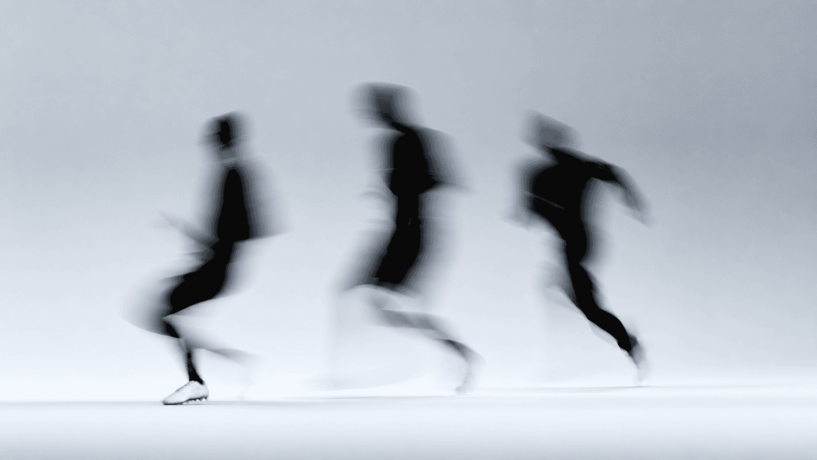 Three people running, captured with motion blur against a light background